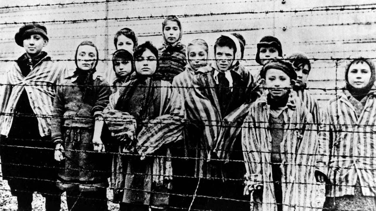 Gruppe von Kindern in KZ-Uniformen hinter einem Stacheldrahtzaun im NS-Konzentrationslager Auschwitz