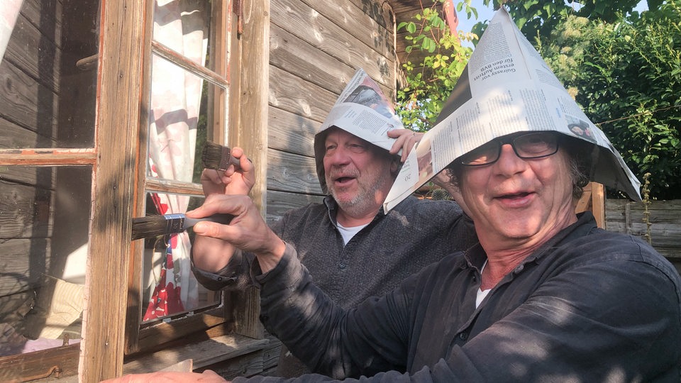 Jens Schellhass streicht mit einem Freund das Fenster eines Gartenhäuschens