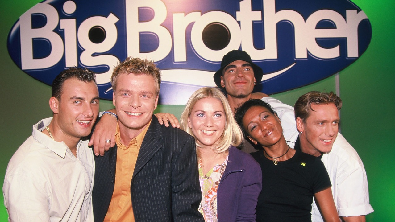 Gruppenbild vor Big Brother-Logo mit den Kandidaten und Moderatoren Zlatko, Oliver Geissen, Aleksandra Aleks Bechtel, John, Andrea und Jürgen Milski