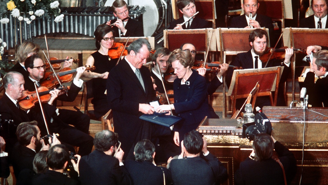 Die Vorsitzende des Nobelpreis-Komitees, Frau Aase Lionaes (Mitte rechts), überreicht dem deutschen Bundeskanzler Willy Brandt die Urkunde und die Medaille des Friedens-Nobelpreises.