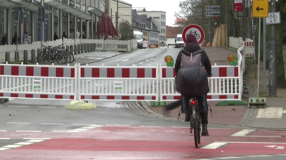 Eine Fahrradfahrerin steht vor der Baustelle der neuen Radpremiumroute Wallring. 