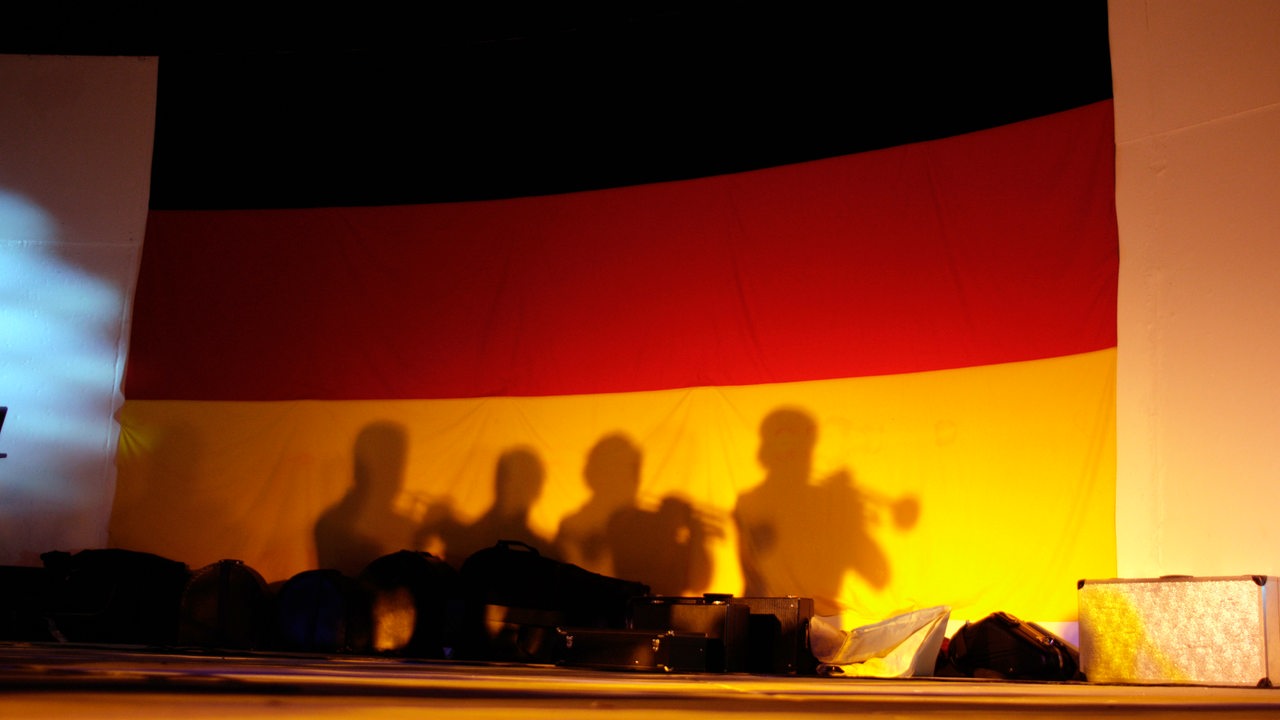 Auf einer Deutschlandfahne sieht man als Schatten 4 Trompeter