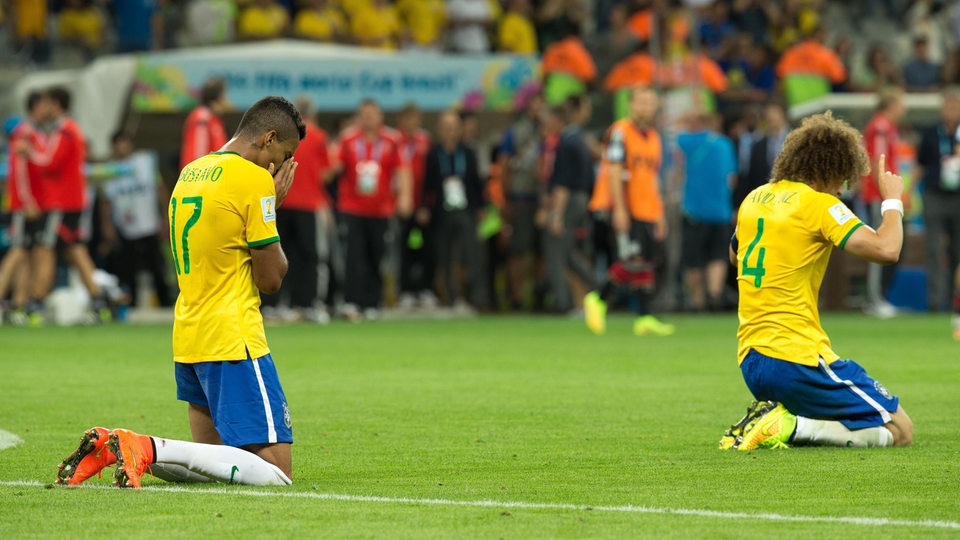 Nach der 7:1 Niederlage von Brasilien gegen Deutschlang im Halbfinale der WM 2014, knien Luiz Gustavo und David Luiz verzweifelt auf dem Rasen.
