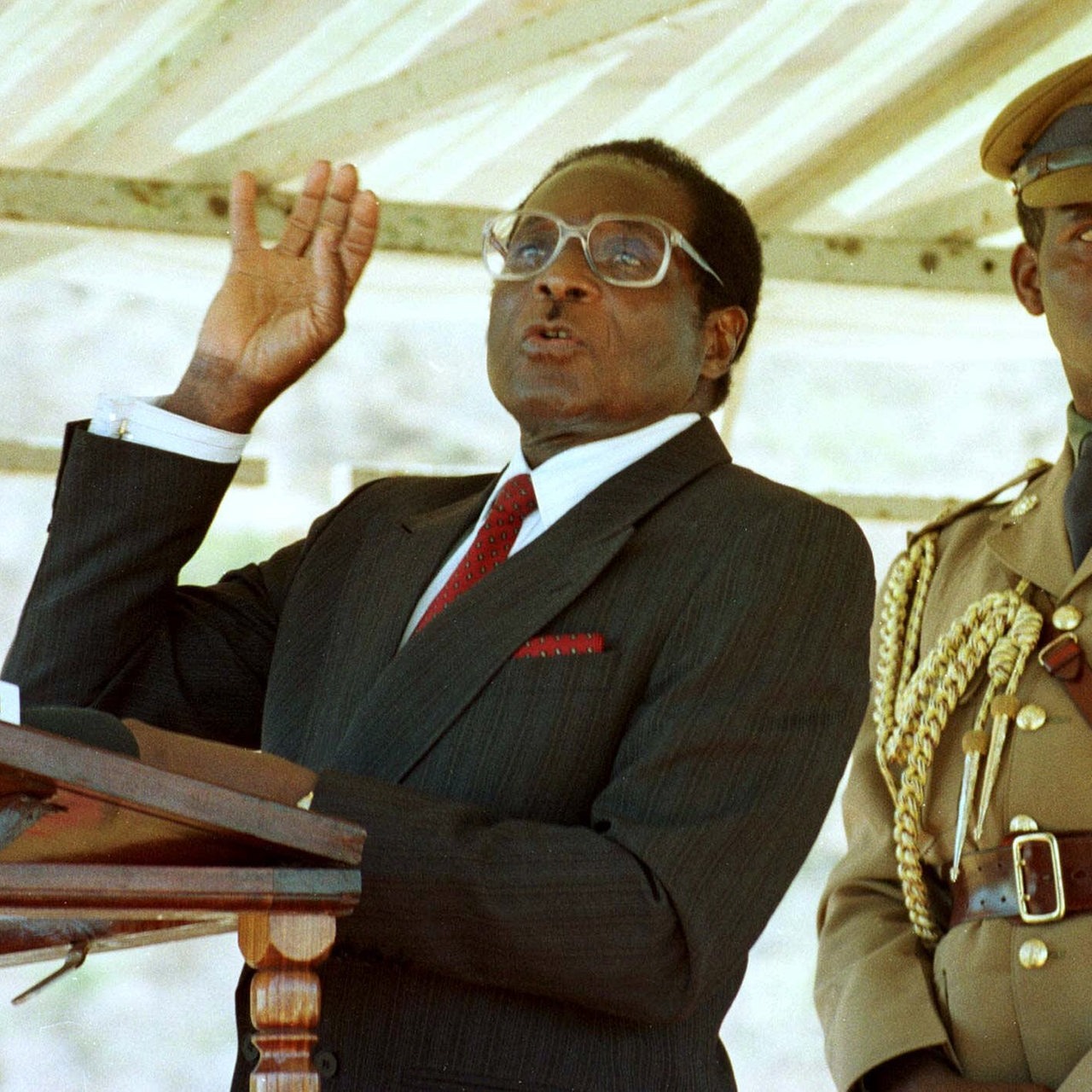 Robert Mugabe spricht am Pult 1998, dahinter ein Militärangehöriger von Zimbabwe