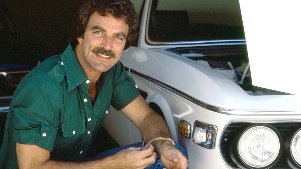 Der Schauspieler Tom Selleck kniet an einem Fahrzeug